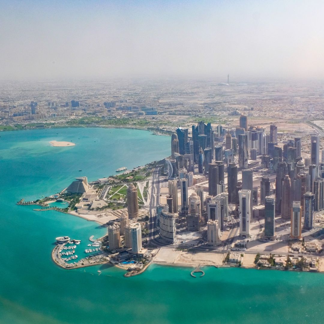 The West Bay skyline of Doha rising along the Corniche at dusk, with the Museum of Islamic Art in the foreground, Qatar's business, finance and sovereign-wealth hub for private jet charter.